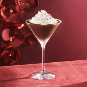 Starbucks Reserve cocktail glass containing beverage topped with whipped cream and pink sprinkles, on a red tablecloth with red backdrop.