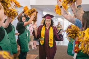 An ASU graduate in cap and gown walking down a row with Starbucks baristas waving pom-poms