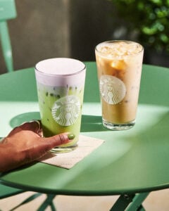 A hand a holding a Starbucks iced matcha with lavender and a glass of iced chai next to it