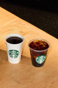 Hot coffee and iced coffee in to-go cups, on a table.