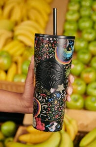 A hand holding a black and colorful reusable cup of FARM Rio and Starbucks collaboration