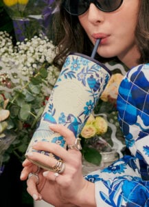 A hand holding a white and blue reusable cup of FARM Rio and Starbucks collaboration