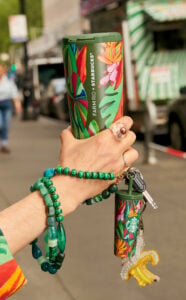 A hand holding a green and colorful reusable cup of FARM Rio and Starbucks collaboration