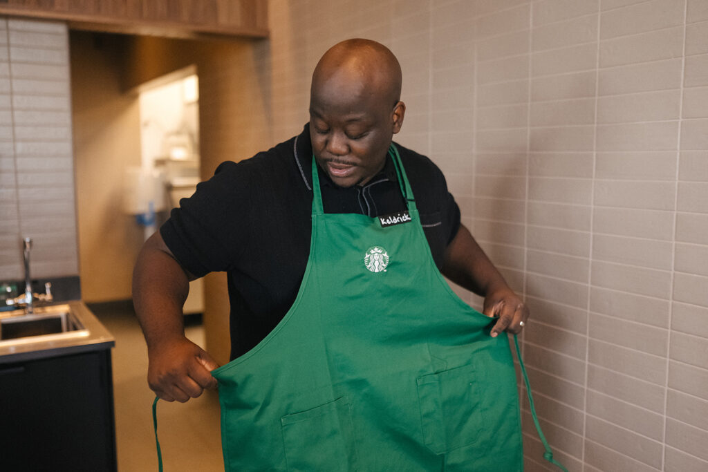 A male Starbucks partner putting on a green apron