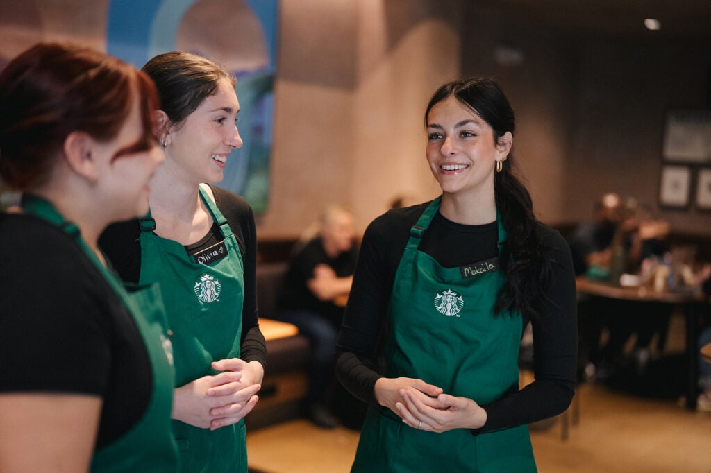 Three Starbucks partners in green aprons standing inside the store having a conversation
