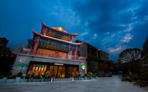 A Starbucks with a traditional Chinese architectural style features vibrant colors and decorative elements. The storefront is adorned with flowers, and a green Starbucks logo is prominently displayed. The sky is a mix of blue and gray, suggesting twilight.