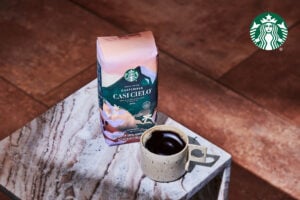 A bag of Starbucks Guatemala Casí Cielo coffee sits on a marble surface next to a speckled ceramic cup filled with dark coffee.