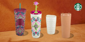 Four colorful Starbucks tumblers are displayed against a textured orange background. The first is a vibrant, patterned tumbler with a purple lid and straw. The second features a floral design with a pink top and a green flower straw. The third is a white, textured tumbler, and the fourth is a sleek, peach-colored tumbler with a lid.