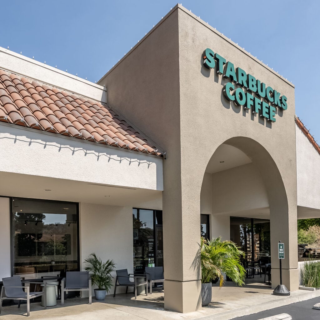 A Starbucks coffee shop with a tiled roof and green signage. Outdoor seating is visible, along with potted plants.