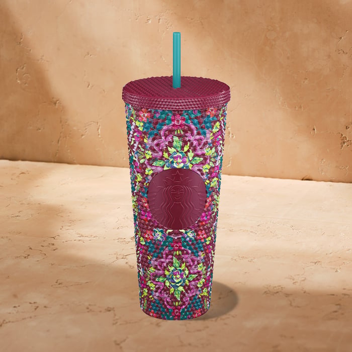 A vibrant, decorative tumbler featuring a floral pattern in shades of purple, green, and blue, topped with a matching lid and straw.