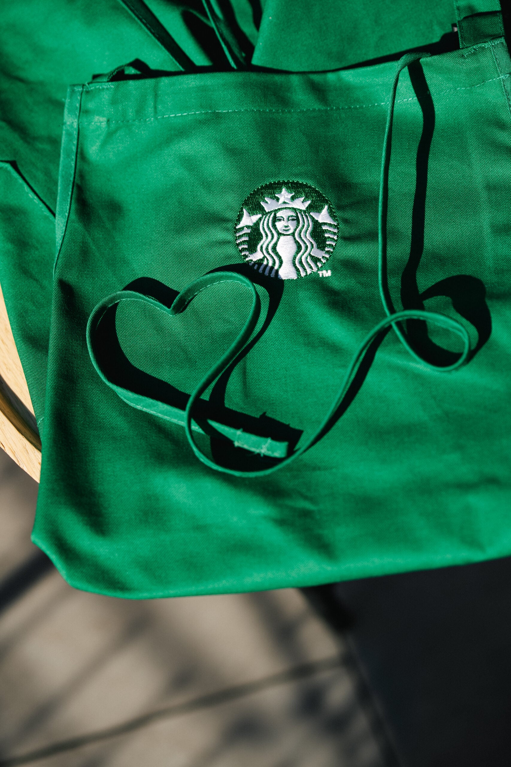 A green apron featuring the Starbucks logo, with a ribbon shaped like a heart laid across it, casting a shadow.