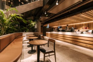 A modern café interior featuring wooden tables and chairs, a curved seating area, and a sleek counter with warm lighting and greenery.