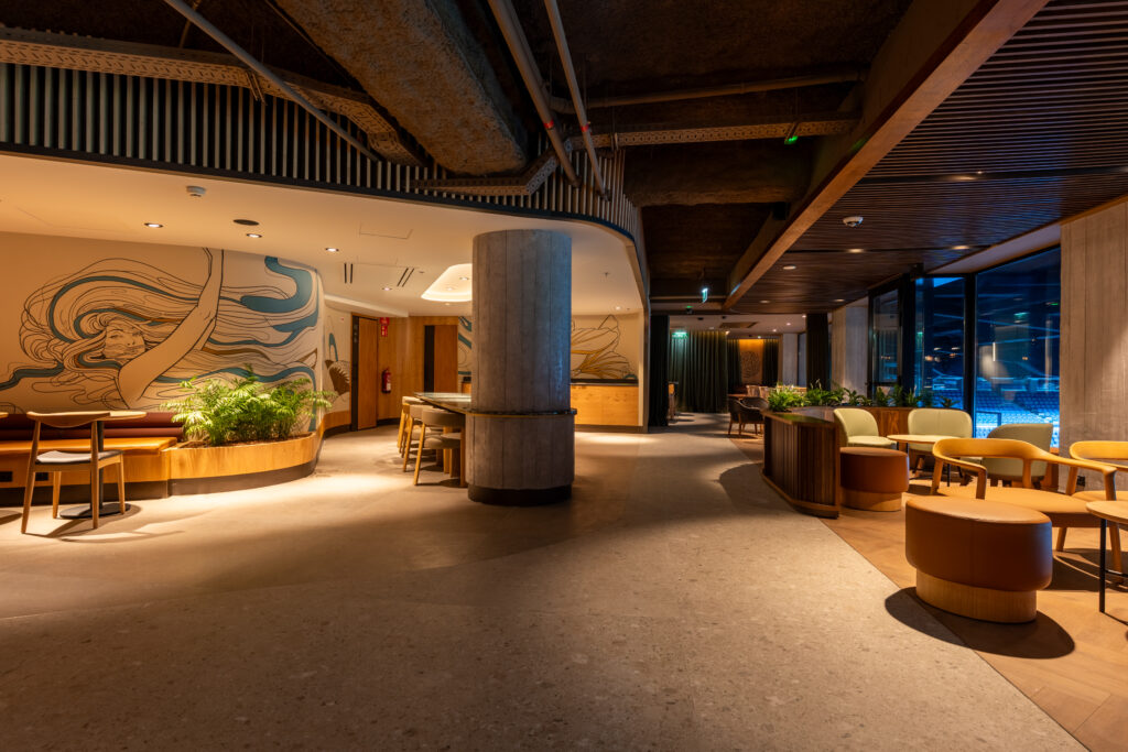 A modern interior space featuring a curved wall with artistic designs, wooden furniture, and greenery. Soft lighting enhances the ambiance.