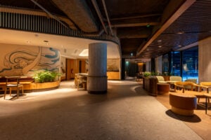 A modern interior space featuring a curved wall with artistic designs, wooden furniture, and greenery. Soft lighting enhances the ambiance.