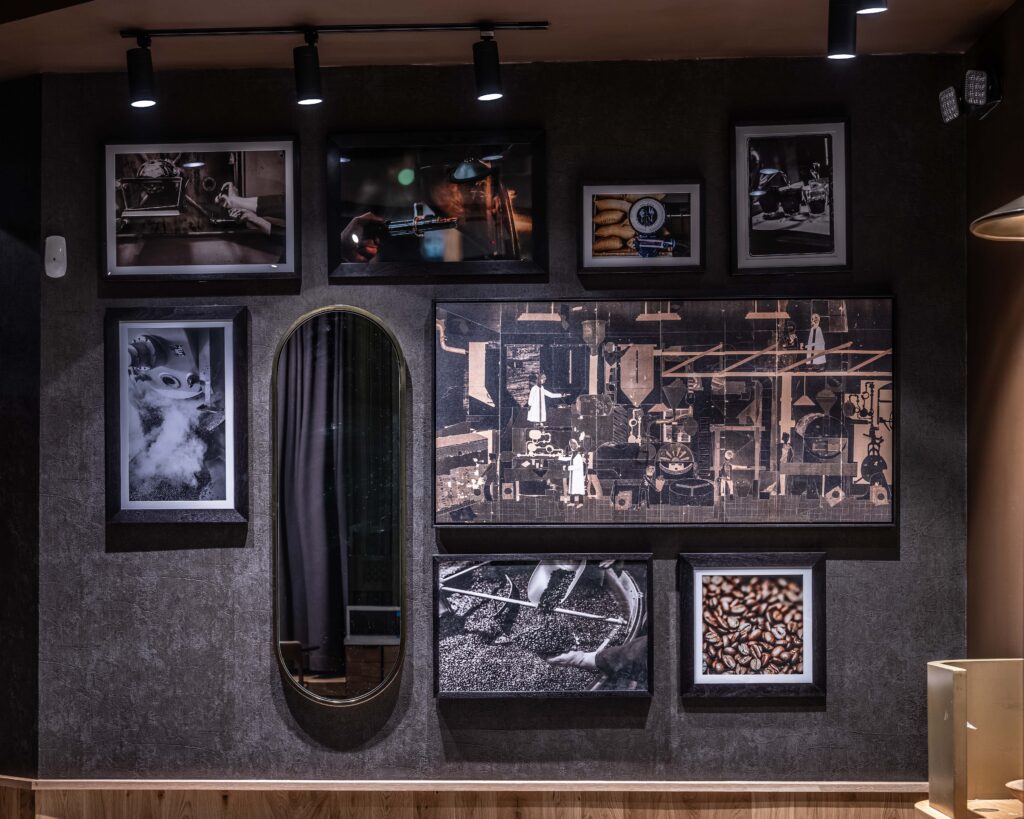 A stylish wall display featuring various framed photographs and artwork, including images of coffee beans, machinery, and a mirror.