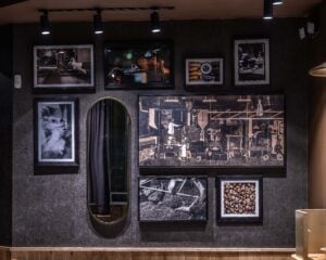 A stylish wall display featuring various framed photographs and artwork, including images of coffee beans, machinery, and a mirror.
