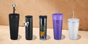 Five stylish tumblers are displayed: a black textured tumbler with a butterfly lid, a sleek black tumbler with a design, a clear tumbler featuring colorful artwork, a purple tumbler with a drip design, and a frosted white tumbler with a geometric pattern.