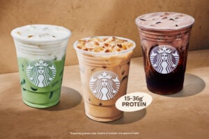 Three iced beverages are displayed: a green drink topped with foam, a light brown drink with ice, and a dark brown drink. Each cup features the Starbucks logo. A note highlights protein content ranging from 15-36 grams.