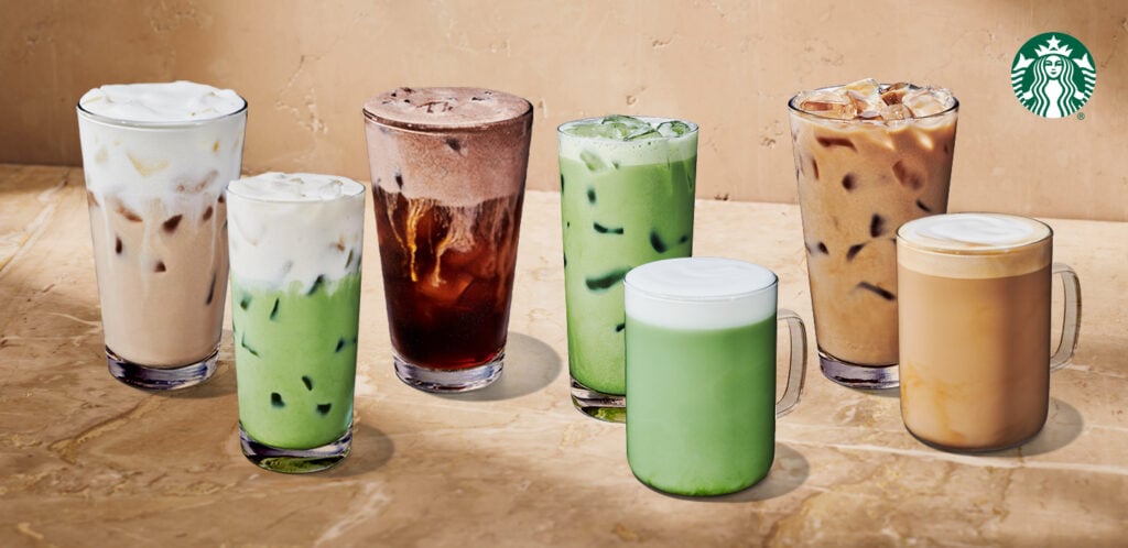 A variety of iced beverages are displayed, including lattes, matcha, and cold brew, in clear glasses and mugs on a textured surface.