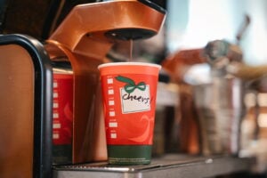 A red coffee cup with a green base and a festive design sits on a counter, with coffee being dispensed into it.