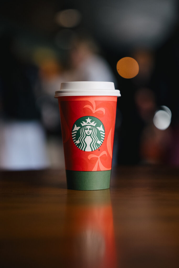 A festive red Starbucks coffee cup with a green sleeve, featuring the logo prominently, sits on a wooden table.