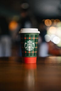 A festive Starbucks coffee cup with a green and red plaid design, featuring the iconic logo, sits on a wooden table.