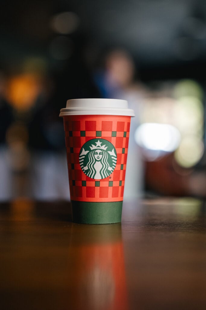 A Starbucks coffee cup with a red and green checkered design, featuring the iconic logo, sits on a wooden table.