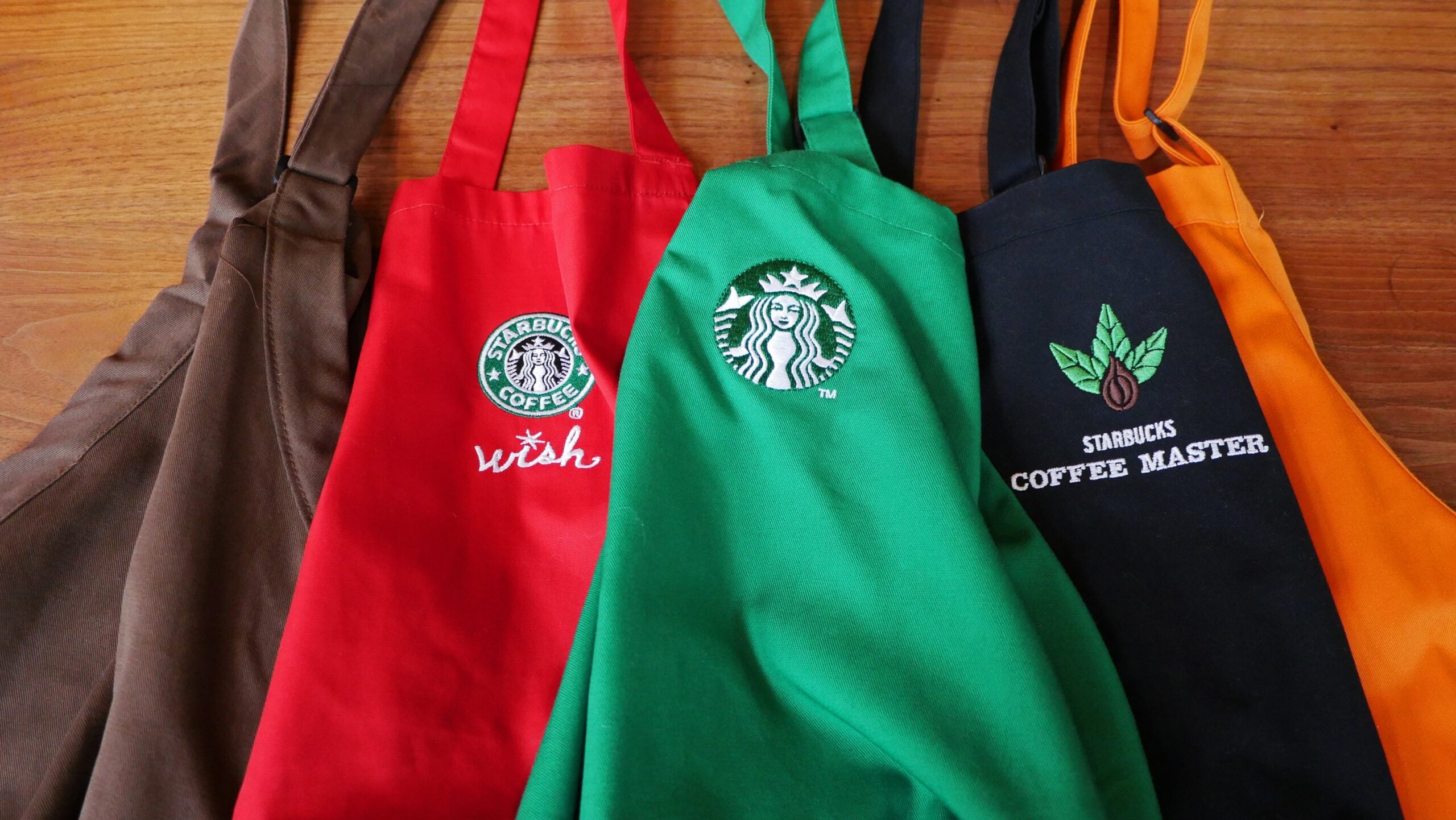 Several aprons in various colors are displayed, featuring Starbucks logos. The colors include red, green, black, and brown.