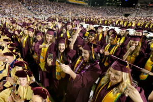 A lively graduation ceremony scene with graduates in maroon caps and gowns, celebrating joyfully, taking photos, and cheering.