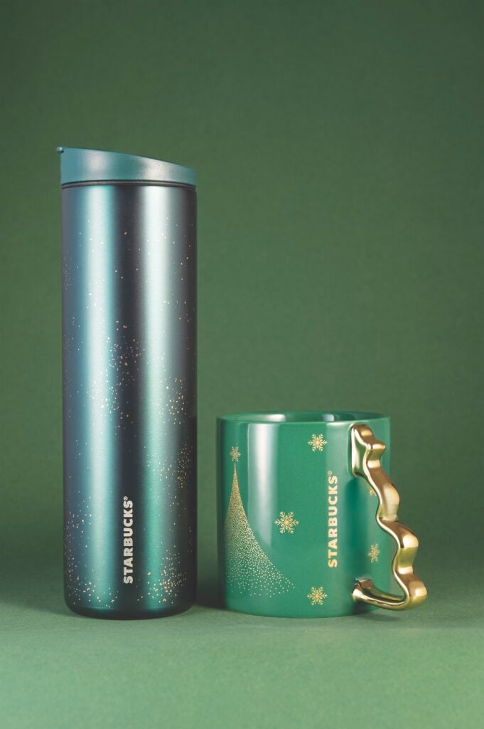 A green Starbucks mug with a gold wavy handle features a Christmas tree design, alongside a sleek, dark teal travel tumbler with sparkles.