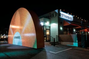 A brightly lit building with a large, glittery orange arch in front, featuring the word "STARBIES" prominently displayed.