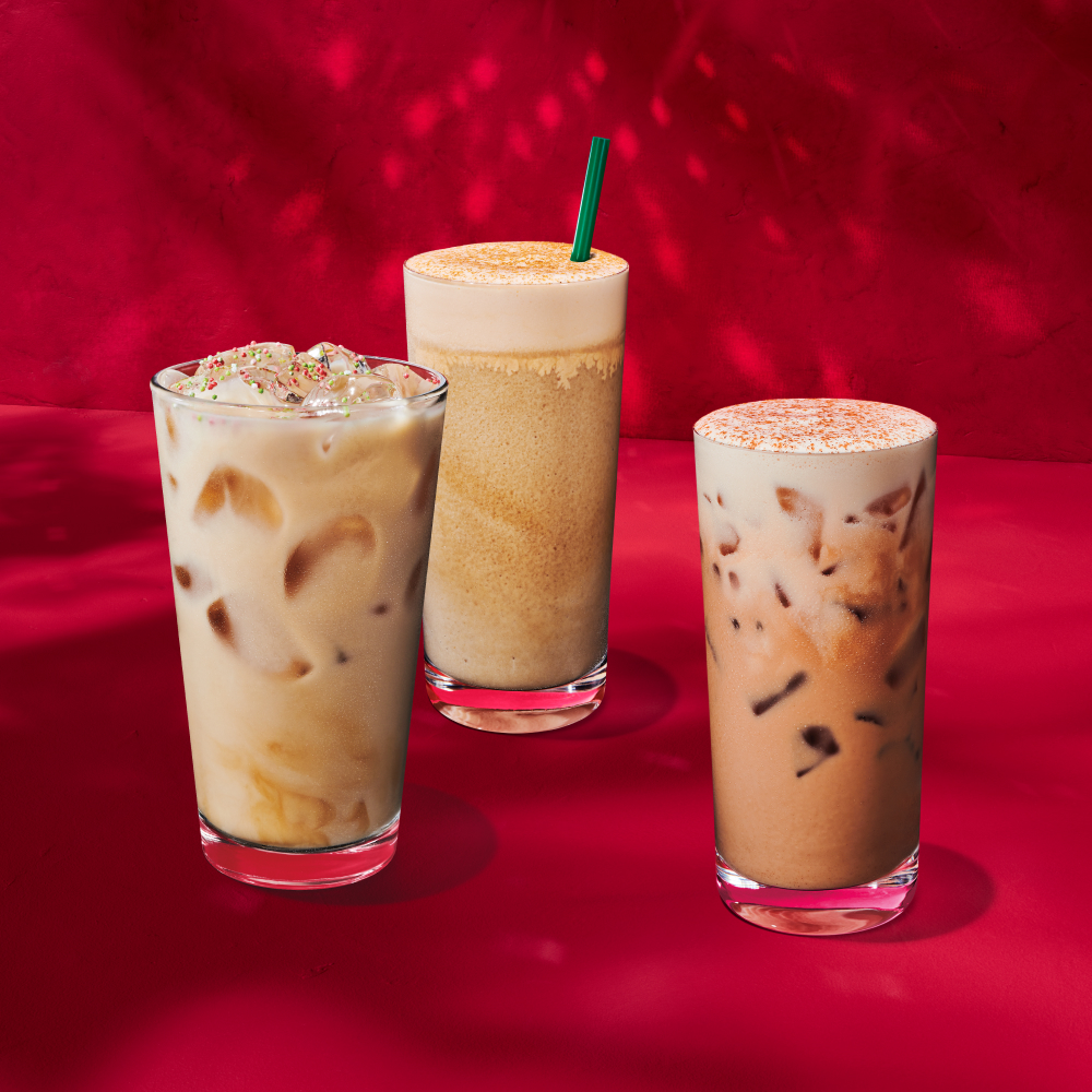 Three iced coffee drinks are displayed against a vibrant red background. The left drink is a light brown iced coffee with ice cubes and festive sprinkles on top. The middle drink is a creamy, blended coffee topped with a sprinkle of cinnamon. The right drink is a darker iced coffee with a frothy top, garnished with a dusting of spice.