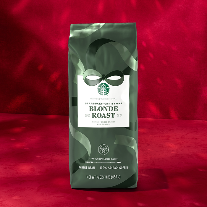 A green bag of Starbucks Christmas Blonde Roast coffee, featuring notes of spiced orange and fig compote, set against a red background.