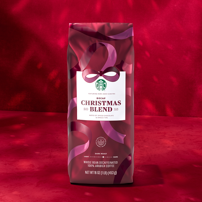 A festive coffee bag featuring Starbucks' Decaf Christmas Blend. The design includes a white label with the blend name, surrounded by decorative ribbons on a red background.