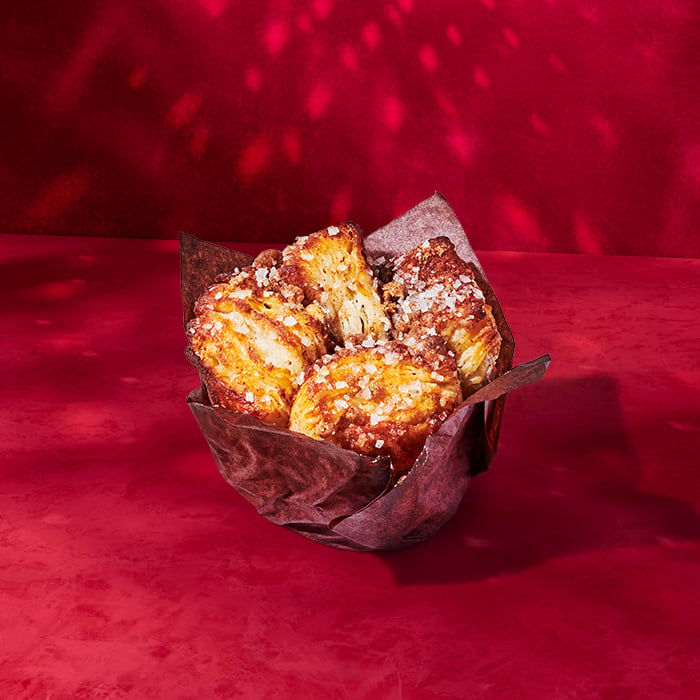 A basket lined with brown paper holds several golden, flaky pastries topped with coarse sugar, set against a red background.