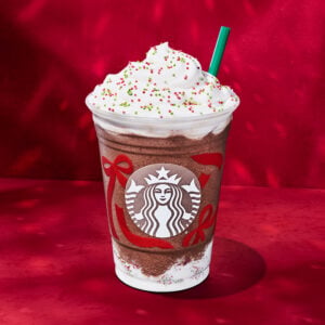 A festive beverage topped with whipped cream and colorful sprinkles, served in a branded cup with holiday-themed decorations.