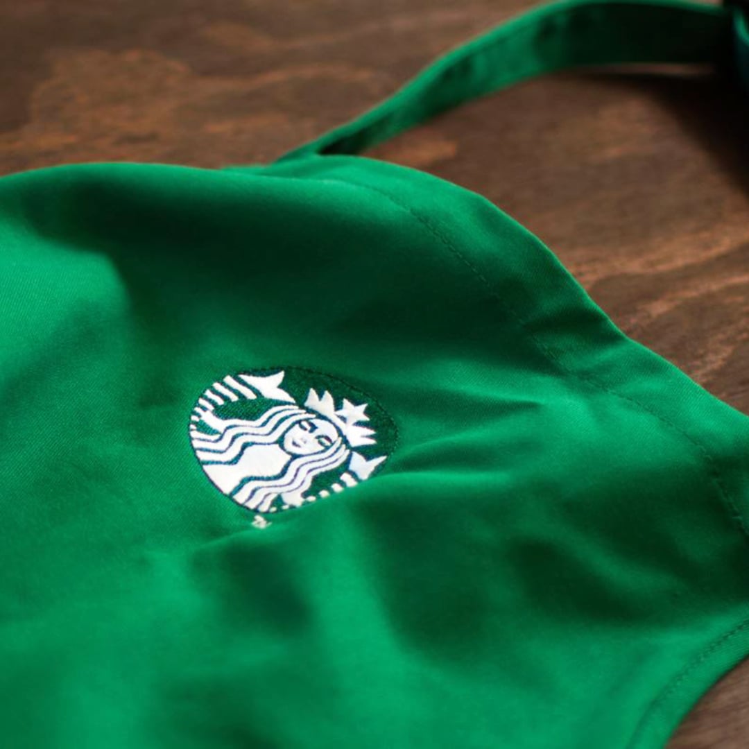 A close-up of a green fabric with a white embroidered logo featuring a mermaid, likely from a coffee shop.