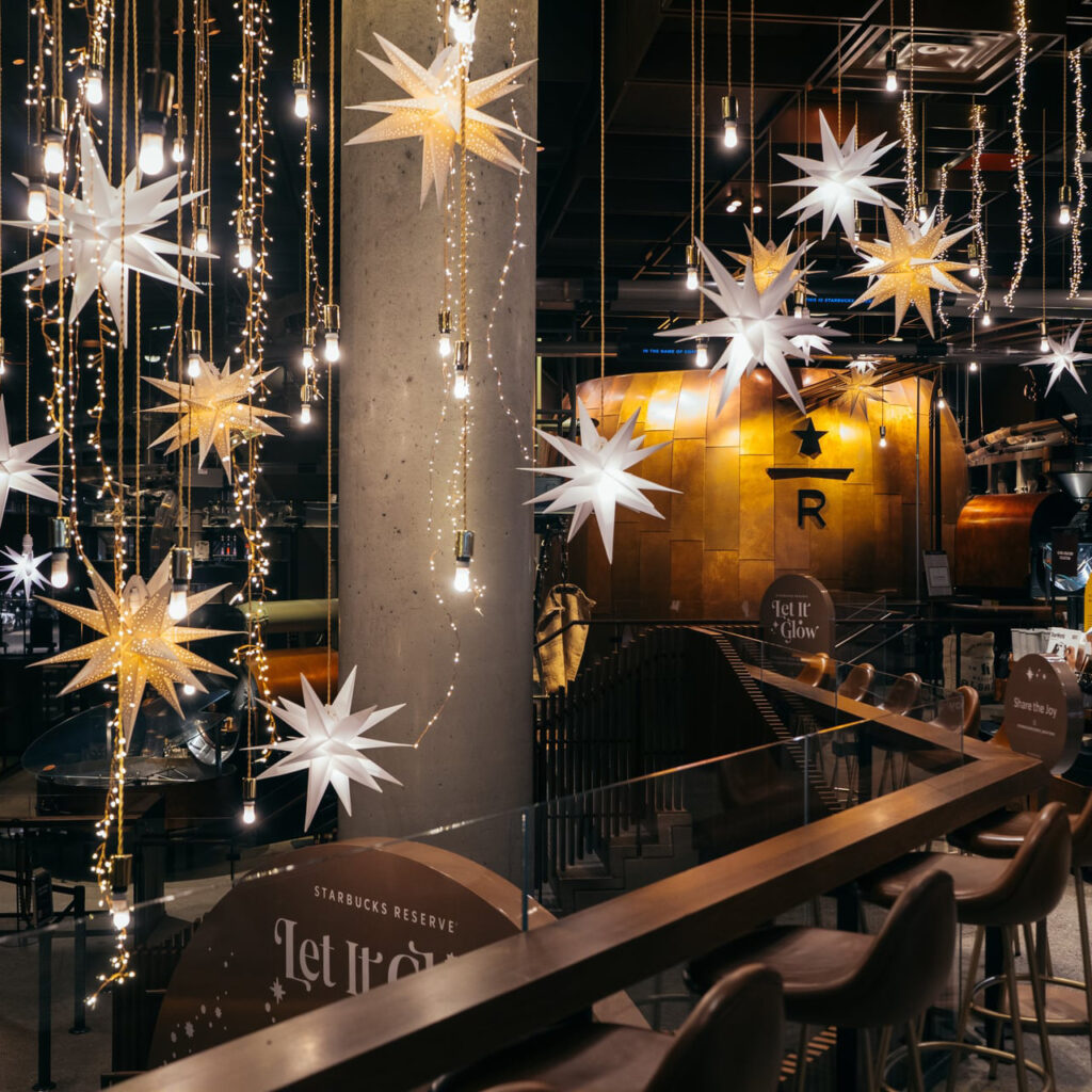 Hanging star-shaped decorations and warm lights create a festive atmosphere in a Starbucks Reserve location, with a stylish interior.