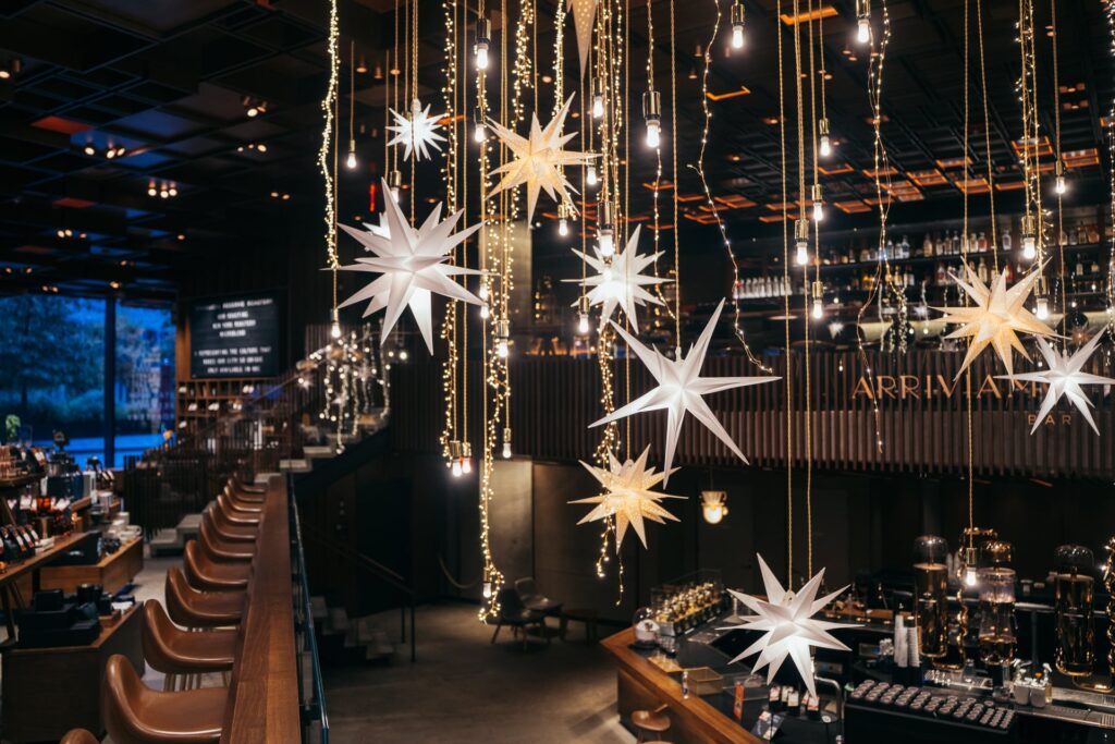 A stylish bar interior featuring hanging star-shaped decorations and warm lighting. The space has wooden accents and a modern design.