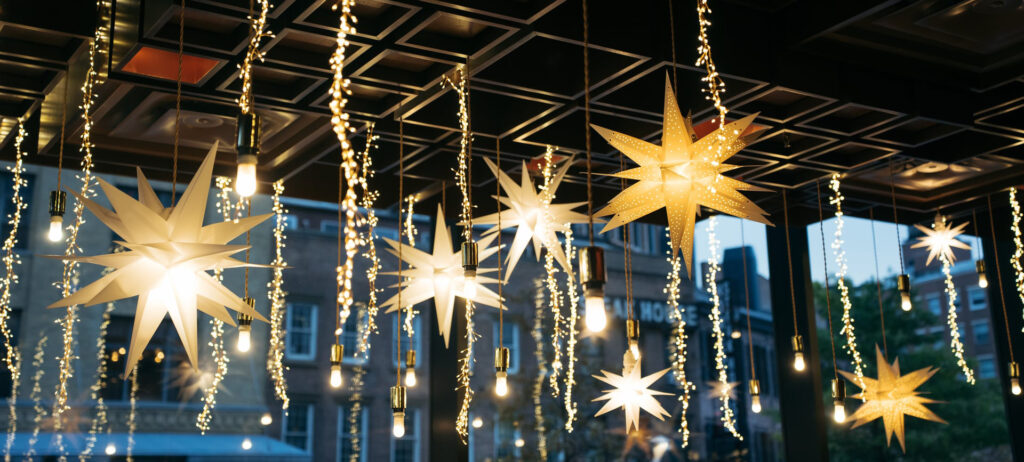 Hanging star-shaped lights and warm bulbs are suspended from a dark ceiling, illuminated by soft fairy lights, creating a cozy atmosphere.