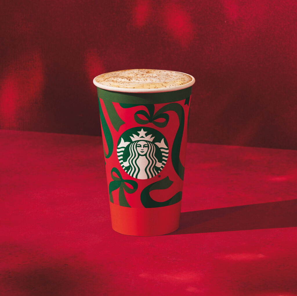 A festive Starbucks cup with a green and red design featuring bows and the Starbucks logo, set against a red background.