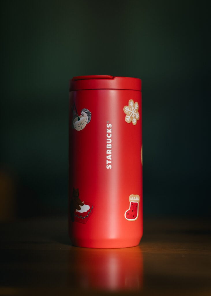 A bright red Starbucks travel mug features festive stickers, including a snowflake, a bear, and a Christmas stocking.