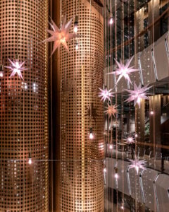 Stylish interior featuring large, perforated copper columns adorned with star-shaped light fixtures and hanging bulbs, creating a modern ambiance.