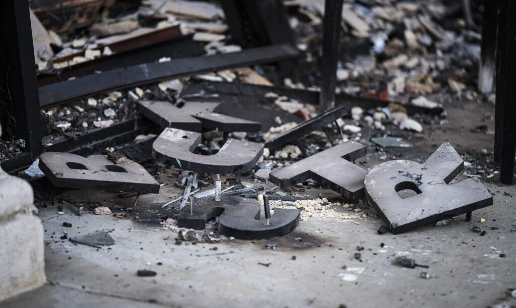 Scattered metal letters lie among debris, including broken concrete and small fragments, on a rough surface.