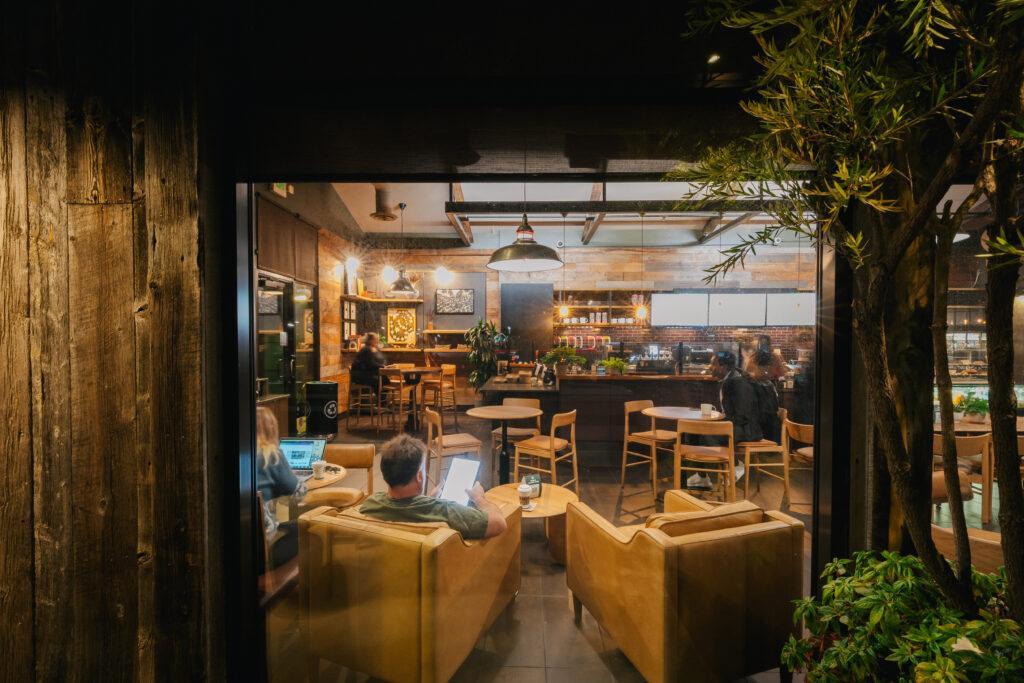 A cozy café scene with warm lighting, featuring wooden decor, comfortable seating, and patrons engaged in various activities.