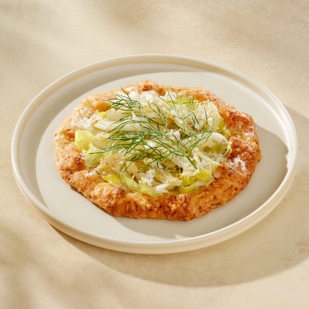 A golden-brown galette topped with shredded cabbage and garnished with fresh dill sits on a light-colored plate.