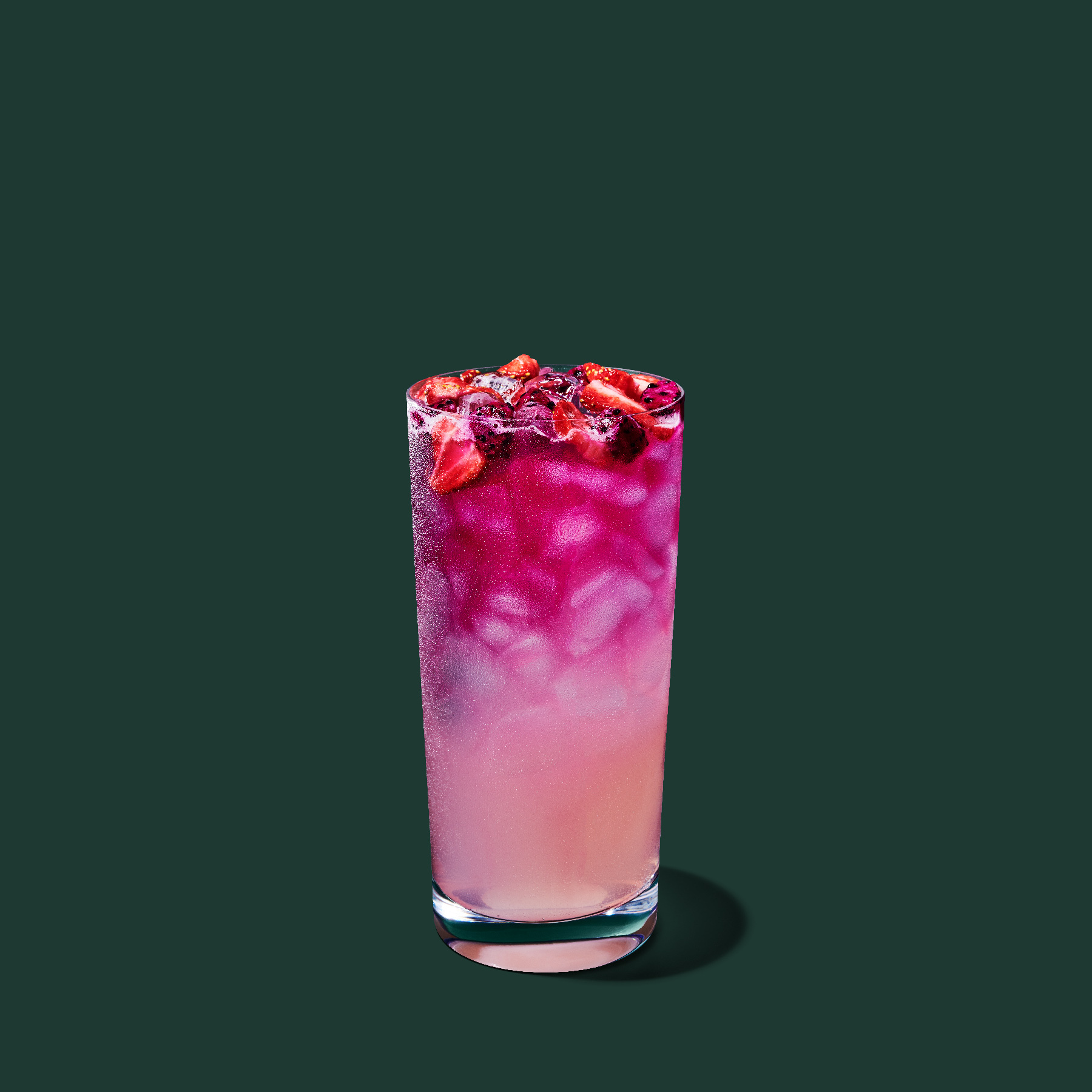 A tall glass filled with a vibrant pink drink, topped with ice and fresh strawberries, set against a dark green background.