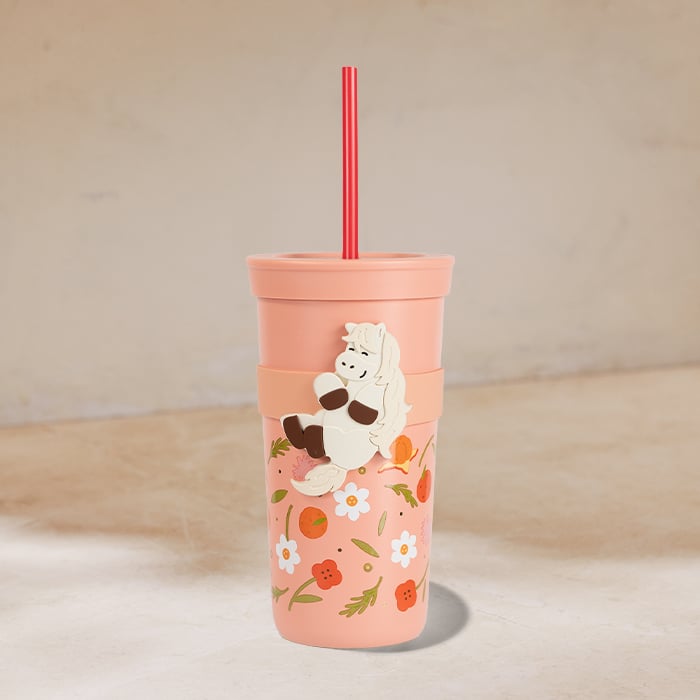 A pink reusable cup features floral designs and a playful character. It has a red straw and a two-part design with a lid.