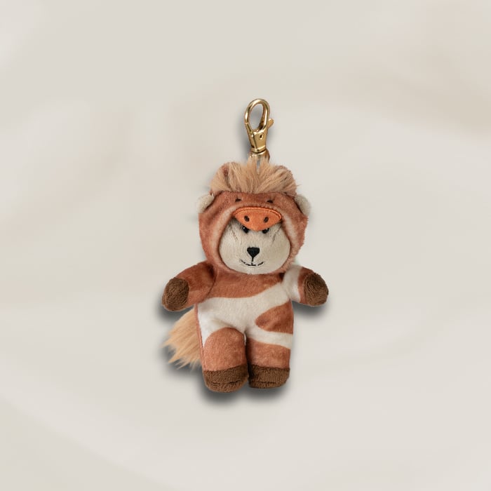 A cute plush keychain featuring a small animal dressed in a brown and white cow costume, complete with a snout and fluffy mane.