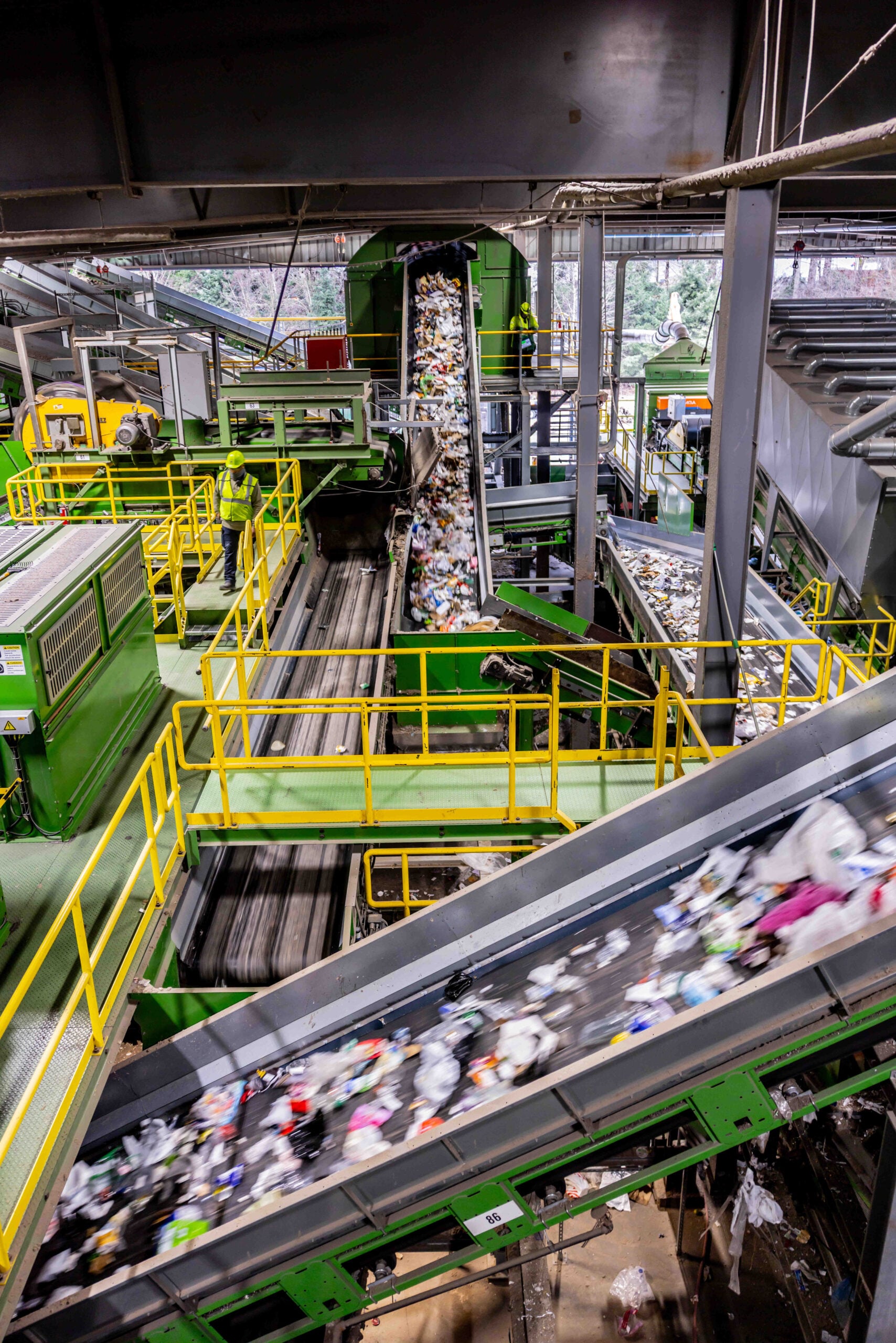 A recycling facility with multiple conveyor belts transporting mixed waste. Workers in safety gear oversee the sorting process.